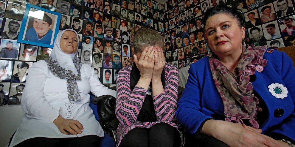 Entourées de photos de personnes disparues, des femmes bosniennes sont rassemblées à Tuzla (Bosnie), dans les locaux de l’Union des mères de Srebrenica, pour regarder la retransmission du procès de Radovan Karadzic par le Tribunal pénal international pour l’ex-Yougoslavie en 2016. © AP Photo/Amel Emric